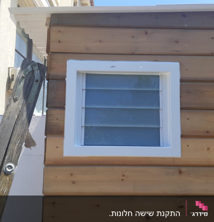 חלון עם תריסי אלומיניום על קיר עץ